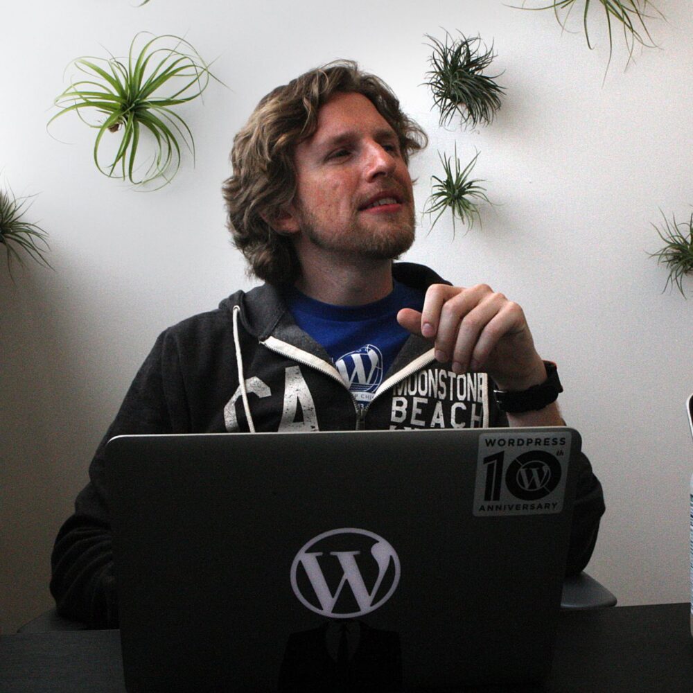 Matt Mullenweg of WordPress company Automattic sits in front of a laptop adorned with a WordPress logo.