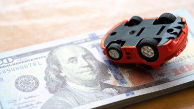 An upside-down toy car on a stack of $20 bills