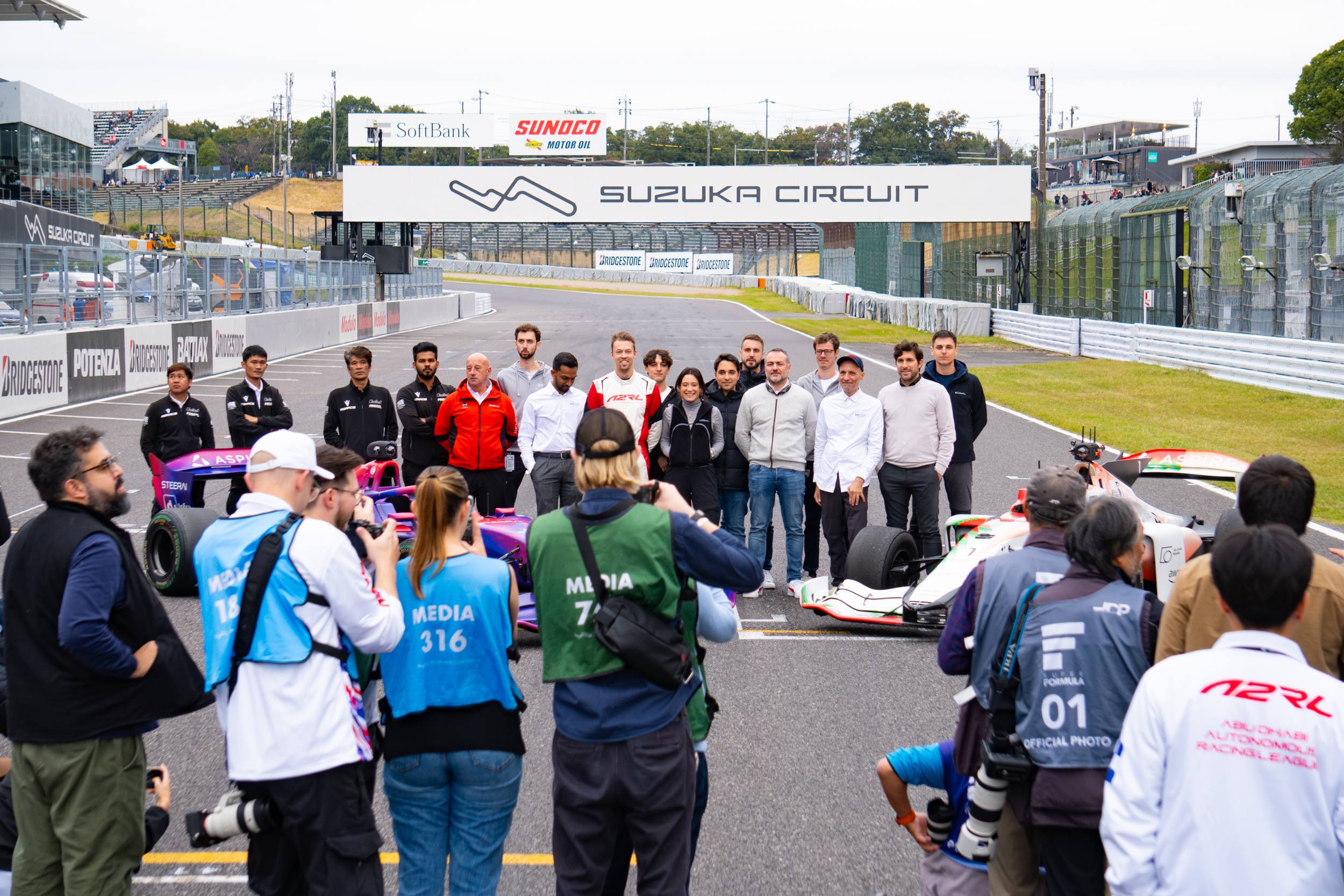 A team of people stand in front of a racing car and pose for a photograph