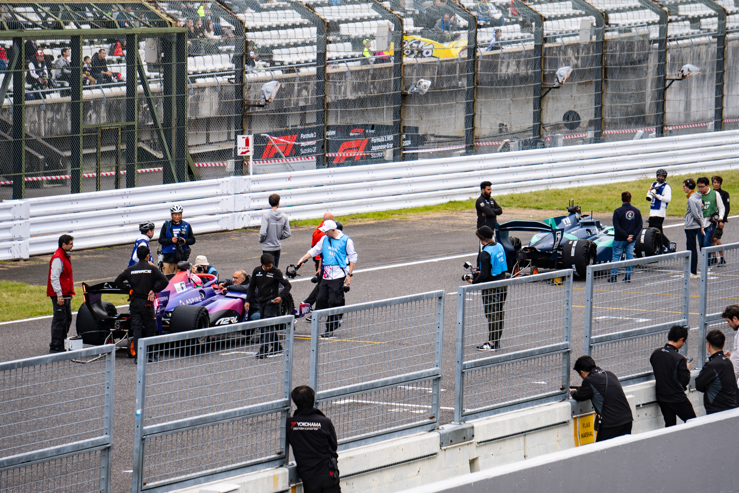 A pair of racing cars on the grid at Suzuka before the start of a race. Photographers and engineers are fussing over the car