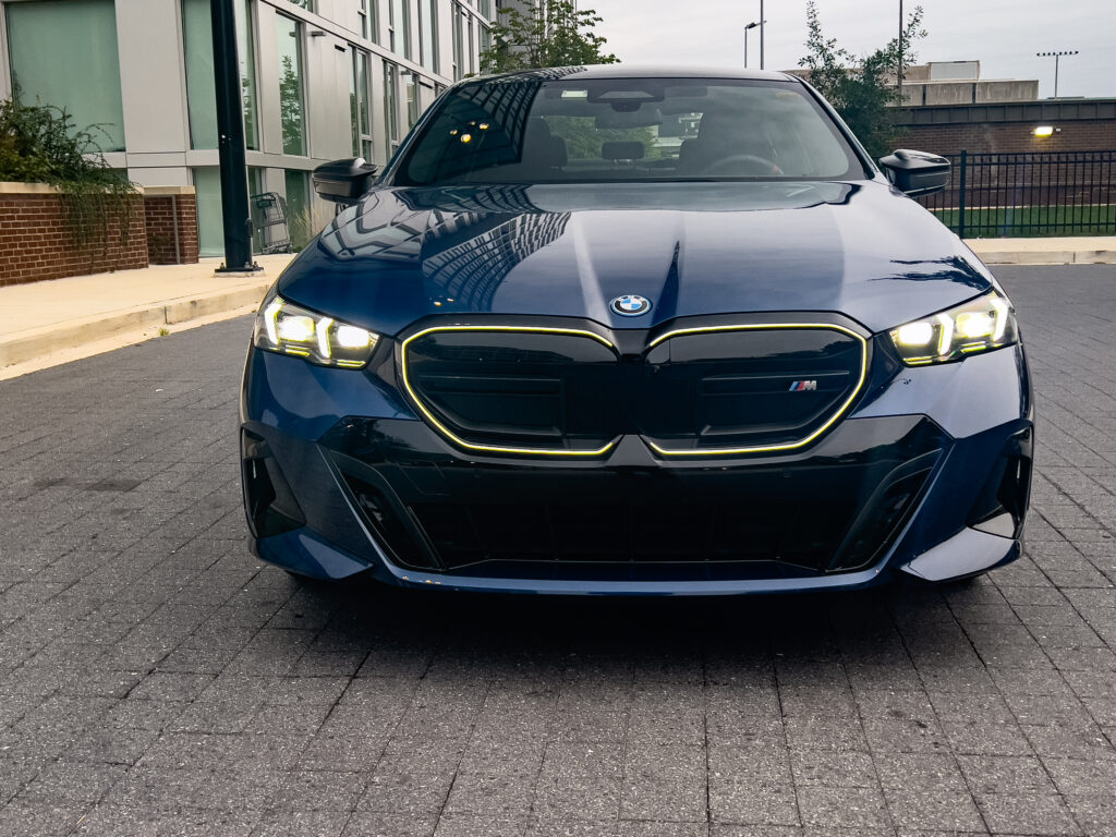 A blue BMW i5 seen head-on, the front grille surround is illuminated white.