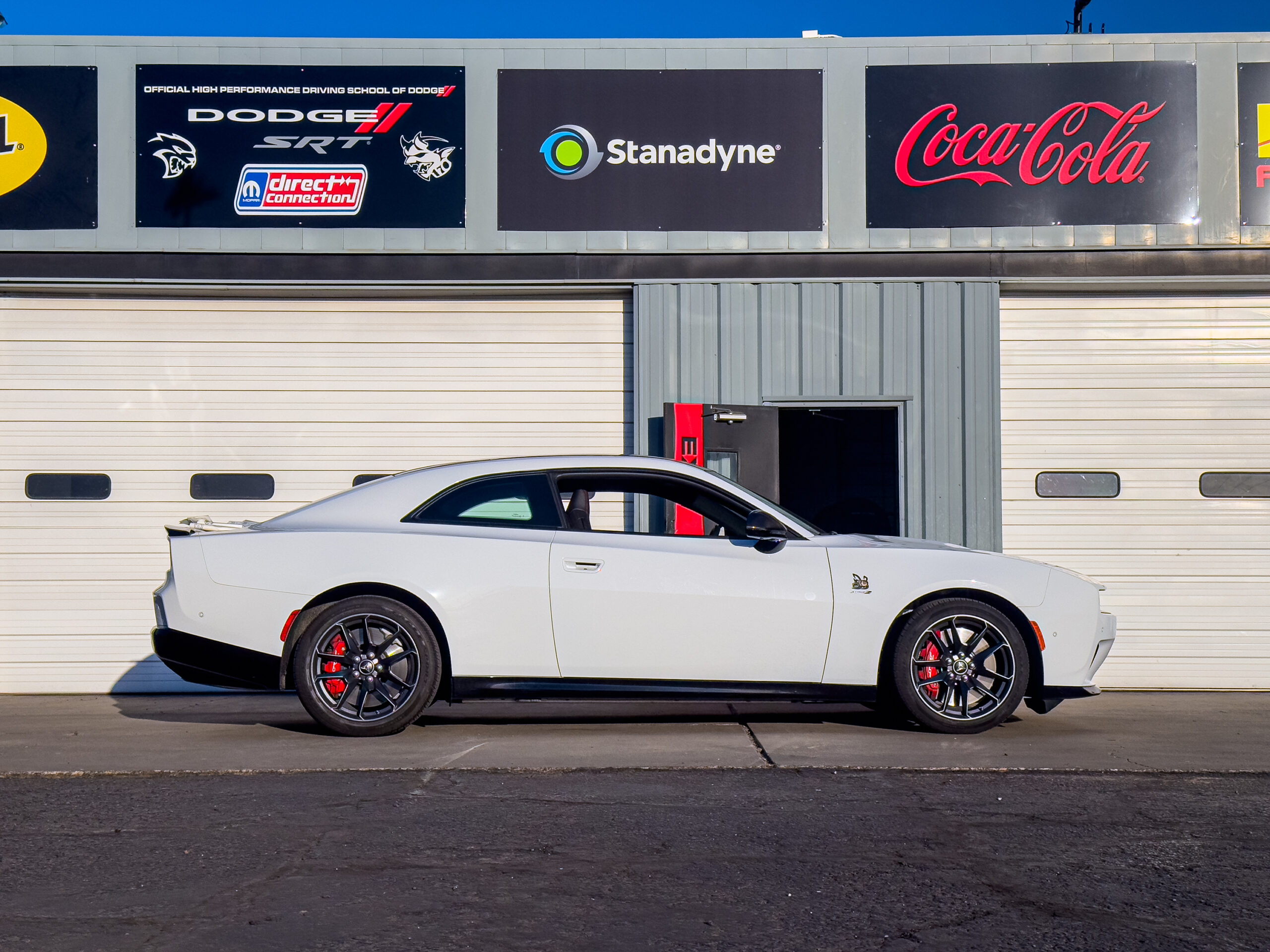 A white Dodge Charger Daytona seen in profile against some garages at a race track