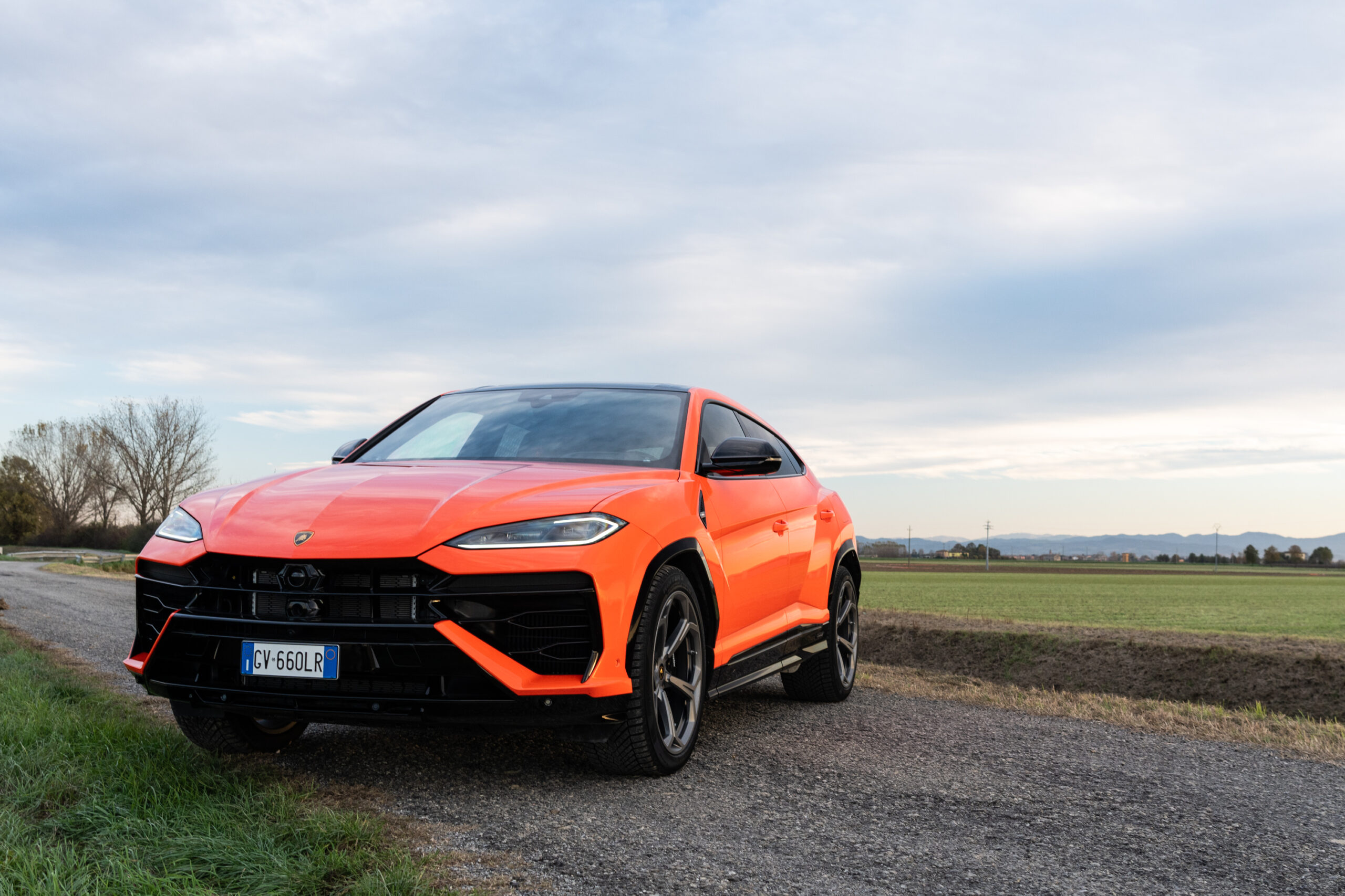 An orange Lamborghini Urus, in a field.