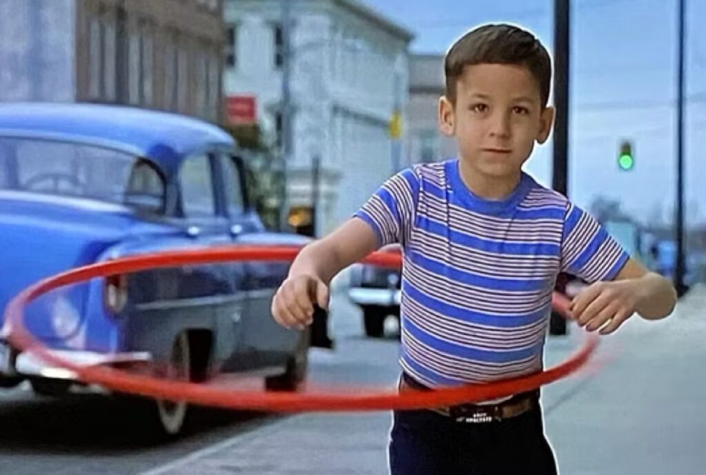 little boy in striped shirt and jeans playing with a hula-hoop