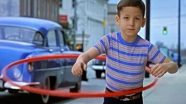 little boy in striped shirt and jeans playing with a hula-hoop