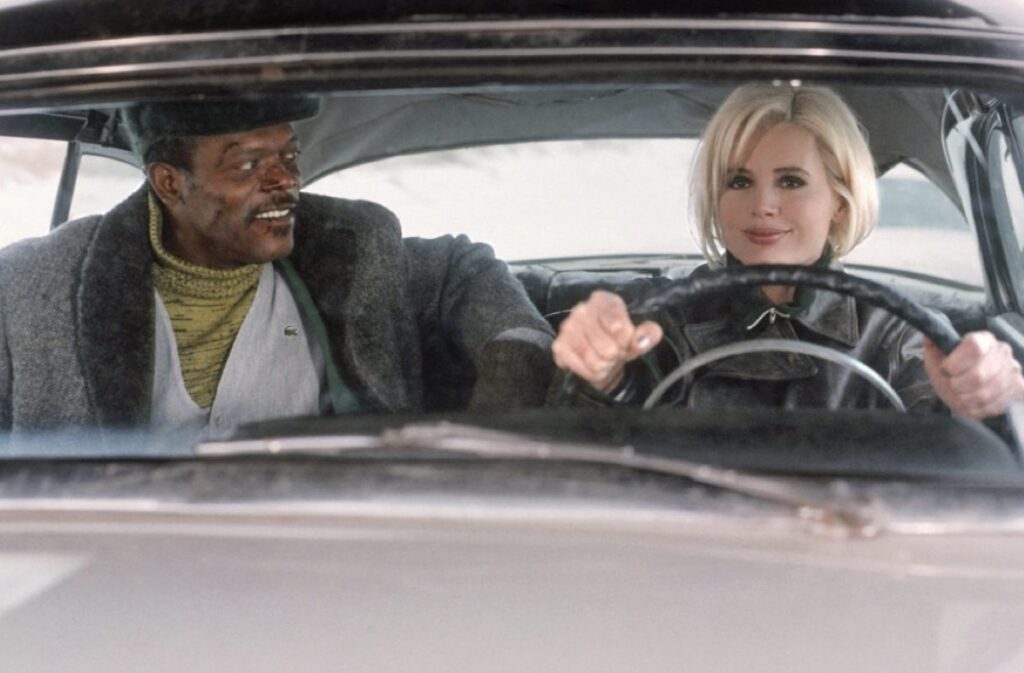 smiling black man in passenger seat of a car driven by blonde woman.