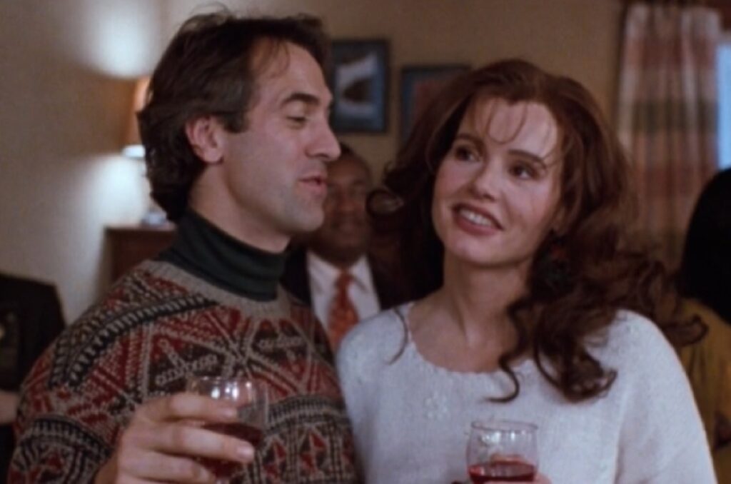 man in a patterned Christmas sweater making a toast at a holiday party while pretty auburn-haired woman looks on.