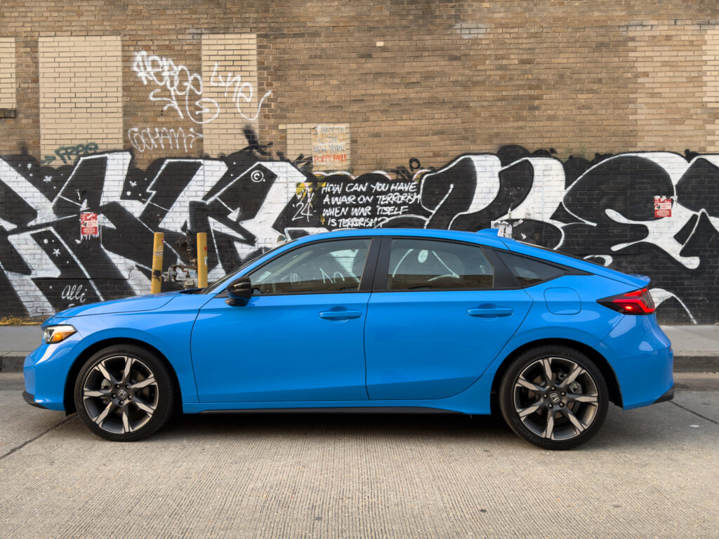 A blue Honda Civic seen in profile parked in front of some graffiti