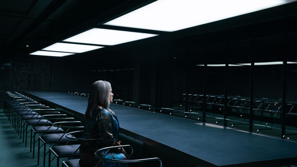 A woman sits alone at a dark conference table