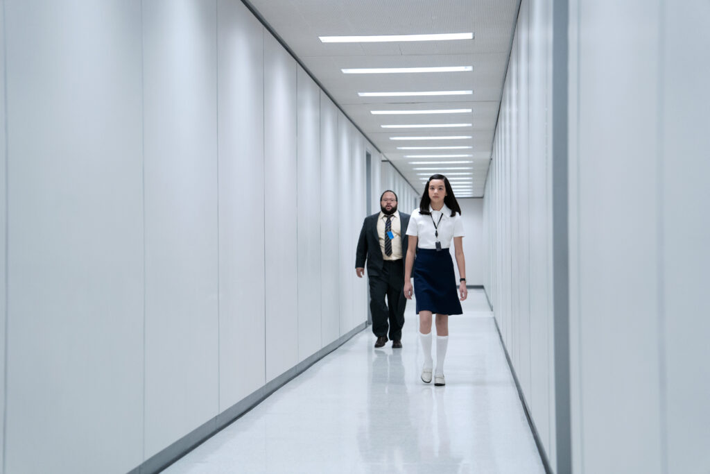 A man and a woman stroll down an austere white hallway