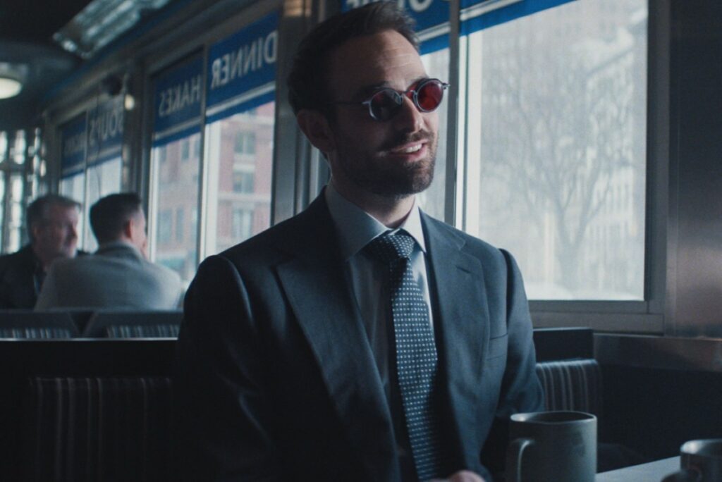 Charlie Cox as Matt Murdock wearing a suit and dark glasses sitting in a diner