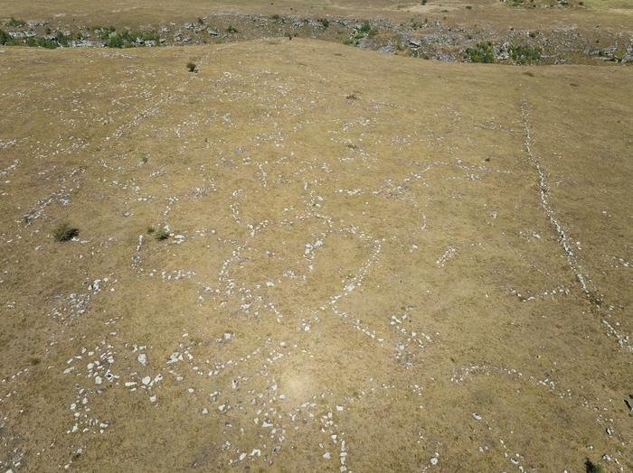 aerial view of a brown landscape with a wall in the distance and the outlines of buried ruins on the ground