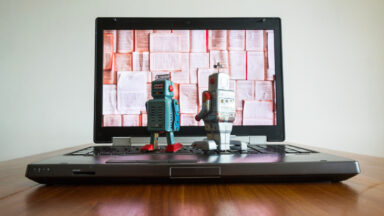 Two tin toy robots looking at laptop screen.