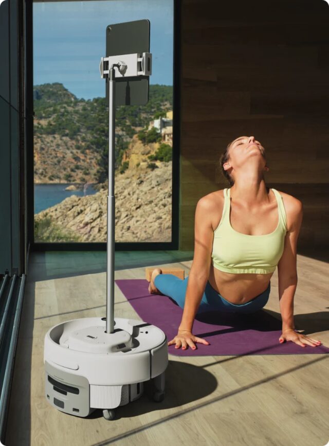 Switchbot K20+ Pro holding up a tablet while a woman does a yoga pose in front of an insanely wealthy-person view of a California cliffside.