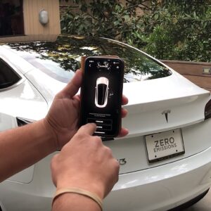 A person holds a smartphone and uses it to summon their Tesla