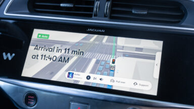 A screen inside a Waymo self-driving car shows an image of cars on the road, information on arrival time, and buttons labeled "Pull over" and "Support."