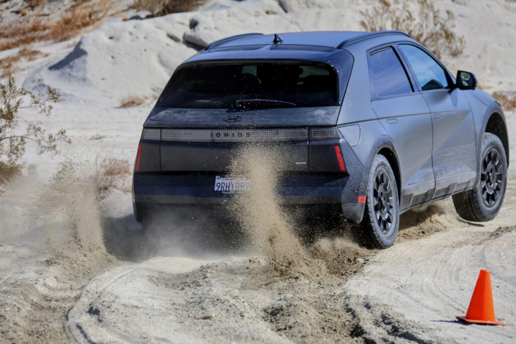 A dark grey Ioniq 5 sends up a spray of sand from its rear wheel