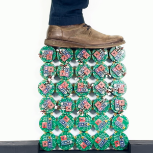 Image of a vertical grid of small electronic devices with a shoe and pants-clad lower leg of someone standing on top of them.