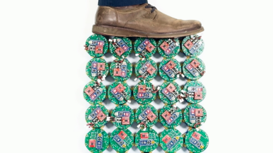 Image of a vertical grid of small electronic devices with a shoe and pants-clad lower leg of someone standing on top of them.