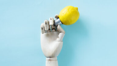 A robot hand holding a lemon-shaped light bulb.