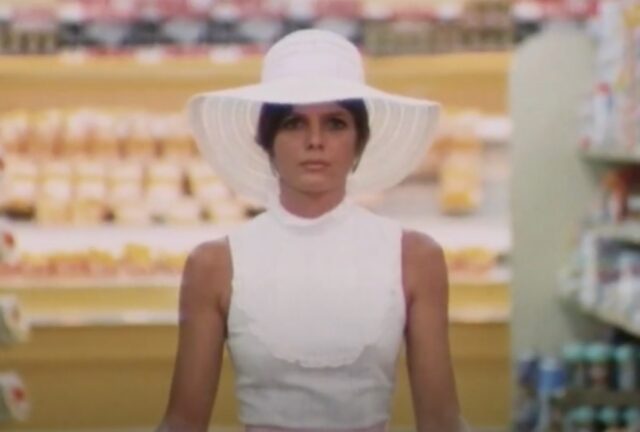 woman in white in big white hat pushing a shopping cart with a blank look on her face