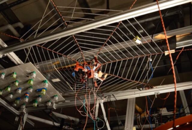 image of a robot spider dangling upside down from a synthetic web