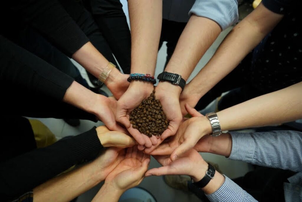 circle of hands with center hand holding coffee beans