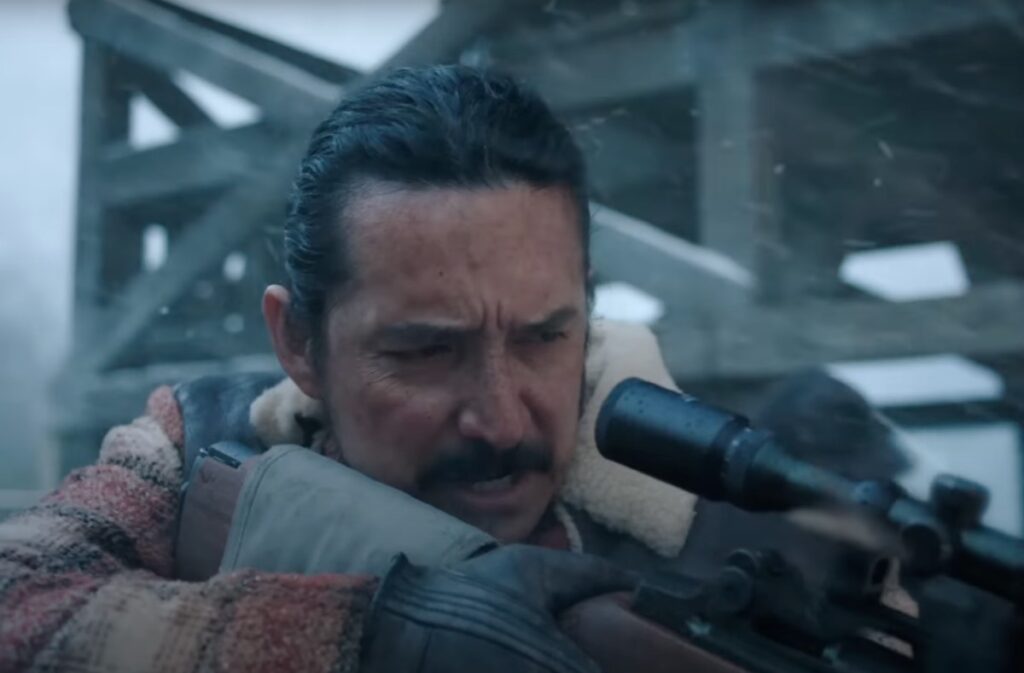 man with mustache firing a rifle in a snowy setting.