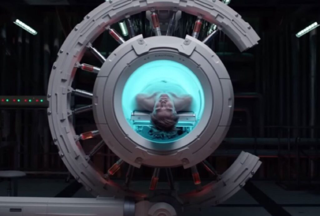 futuristic circular machine (like an MRI) with a body coming out head first from the center