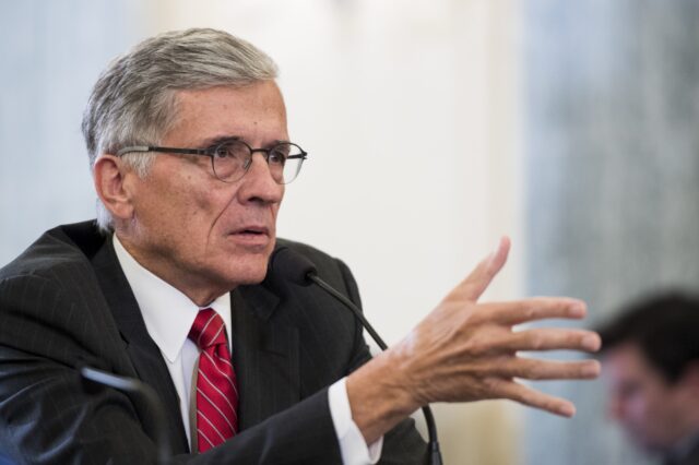 Then-FCC Chairman Tom Wheeler sits at a table and speaks in front of a microphone during a Senate hearing.