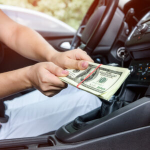 Female hands giving dollar bundle inside car close up