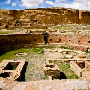 Image of a large, circular, below-ground area surrounded by very finely crafted stone walls. Other ruins are in the background.