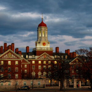 An image of a red brick building with a spire, taken at dusk, with dark grey clouds in the background.