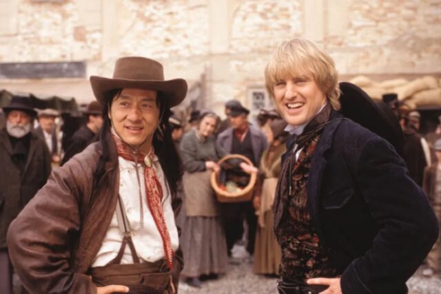 asian man with long hair in a cowboy hat with hands on hips, a stance mirrored by blonde man standing next to him on the right, in a 19th century suit