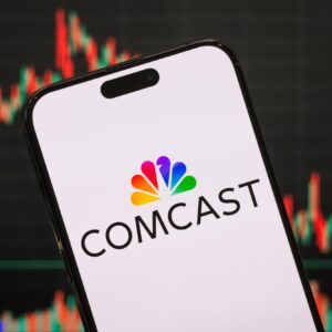 A Comcast logo displayed on a smartphone screen with a stock chart in the background.