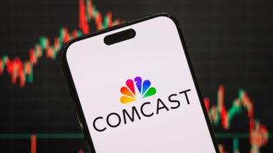 A Comcast logo displayed on a smartphone screen with a stock chart in the background.