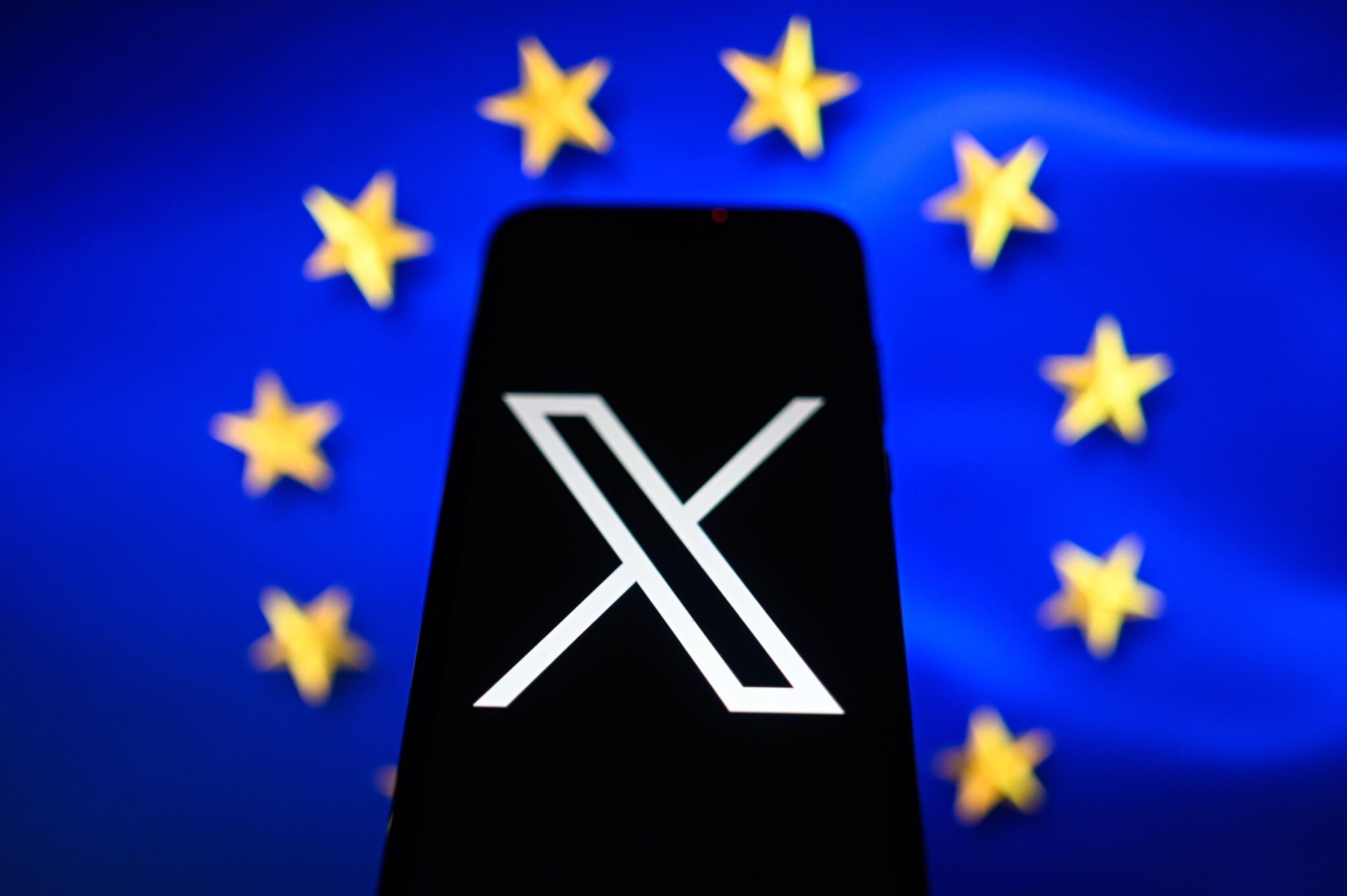 In this photo illustration an X logo is displayed on a smartphone with the European Union flag in the background.