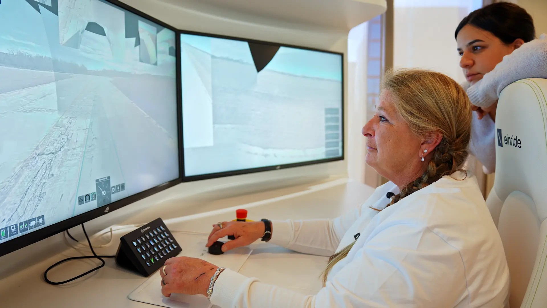 A woman monitors a video feed of an autonomous truck. A younger woman stands to her side.