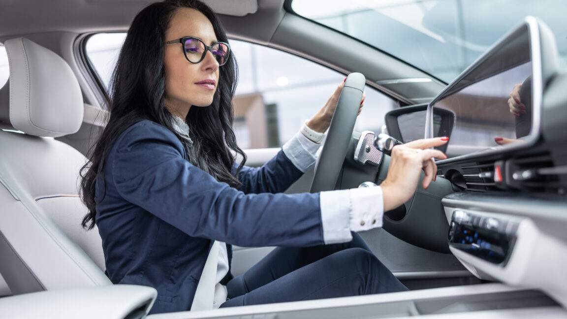 Woman in business clothes touches the infotainment panel screen in her electric vehicle.