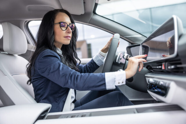 Woman in business clothes touches the infotainment panel screen in her electric vehicle.