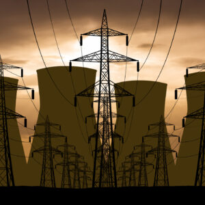 An orange, cloudy sky backlights a set of electrical wires on large pylons, leading away from the cooling towers of a nuclear power plant.