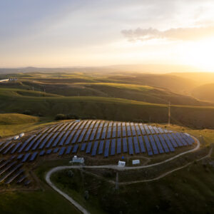 A view of a hlltop lit by the rising sun, with solar panels covering it.