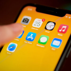 Thumb hovering over the Apple App Store icon on an iPhone with an orange backgbround.