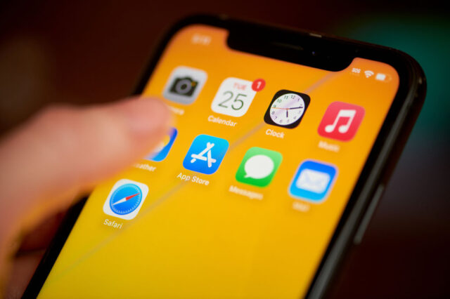 Thumb hovering over the Apple App Store icon on an iPhone with an orange backgbround.