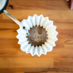 Hot water being poured into a pour-over container, seen from above, as the coffee grounds are blooming.