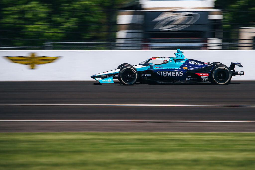 Kyle Kirkwood's indycar drives past the IMS logo on one of the track walls.