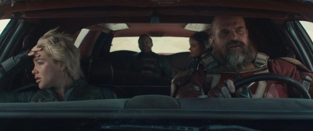 Man in Red Guardian suit driving a limo while blong woman in front seat looks out passenger window in boredom