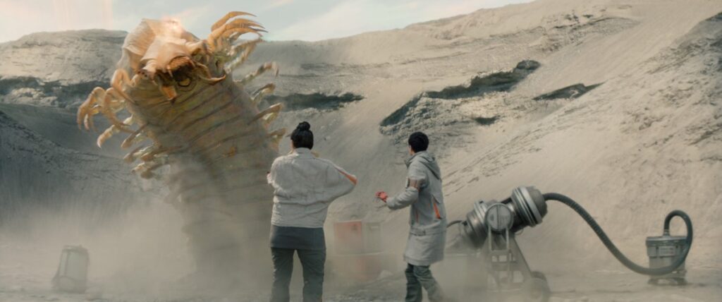 two female scientists on a desert planet react in horror as a giant wormlike monster rears out of the ground.
