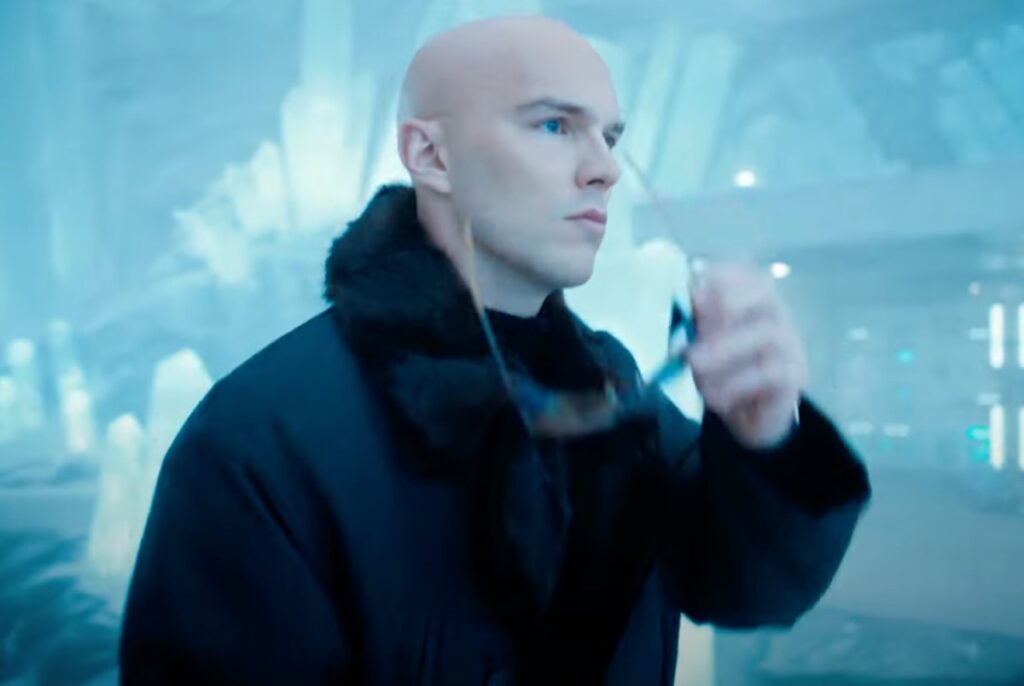 Bald man clad in black striding into an icy fortress while removing dark glasses.