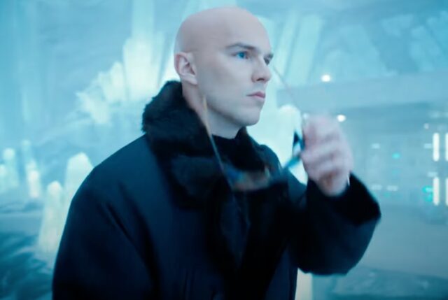 Bald man clad in black striding into an icy fortress while removing dark glasses.